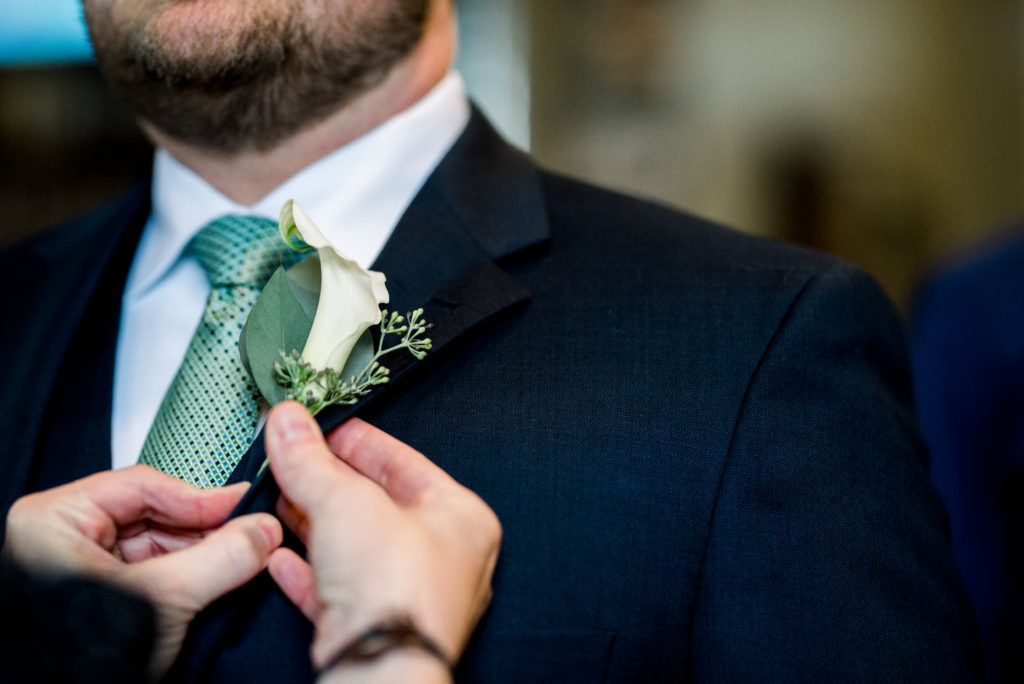 Wedding planner pinning on the groom's boutonniere before the wedding ceremony.