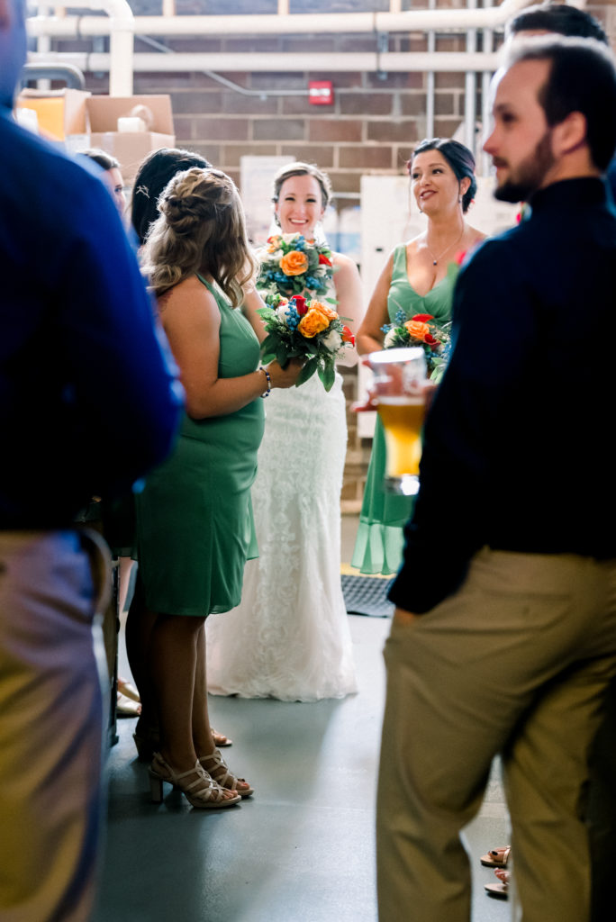 Bride with her bridal party hiding behind the fermentation tanks in the 1915 Room of Moontown Brewing Company before the ceremony started.