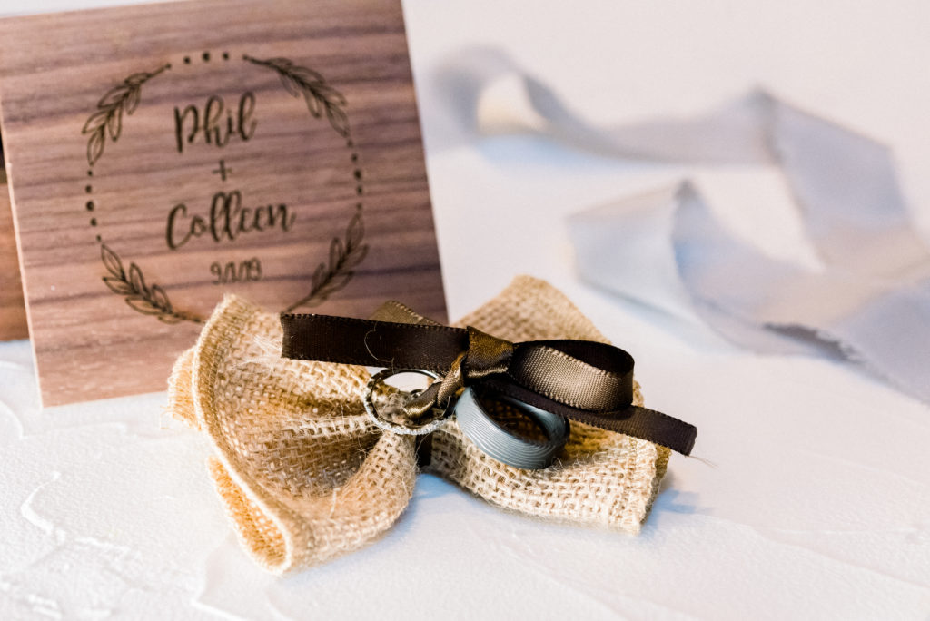 Detail photo of the bride and groom's wedding bands tied to a burlap bow and styled in front of the wooden box the couple had made for their wedding day.