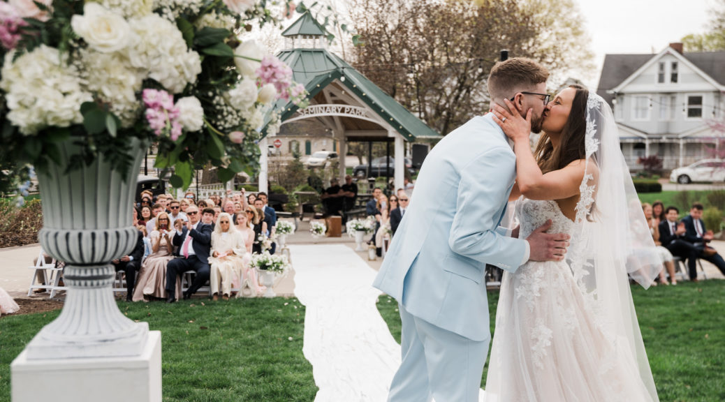 Bride and Groom's first kiss at Seminary Park from behind so that the couple's families' reactions are visible in the photo.